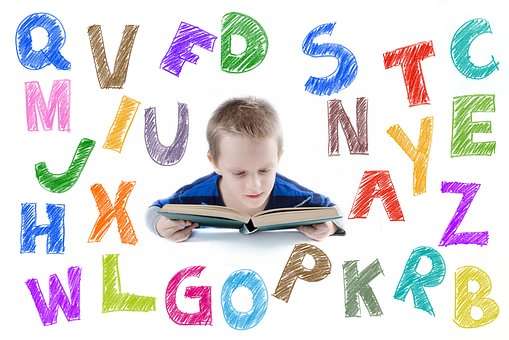 Kind liest in einem Buch. Zu sehen sind Viele Großbuchstaben mit Buntstiften gemalt.